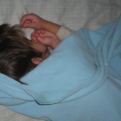 Get kids to bed earlier is easier when you follow these simple steps. Image of a little boy sleeping on his bed, covered by a light blue blanket.