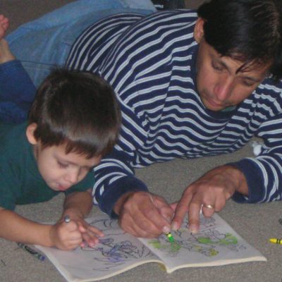 Plan kids date nights with your children. Image of young boy and his father laying on the floor coloring in a coloring book.