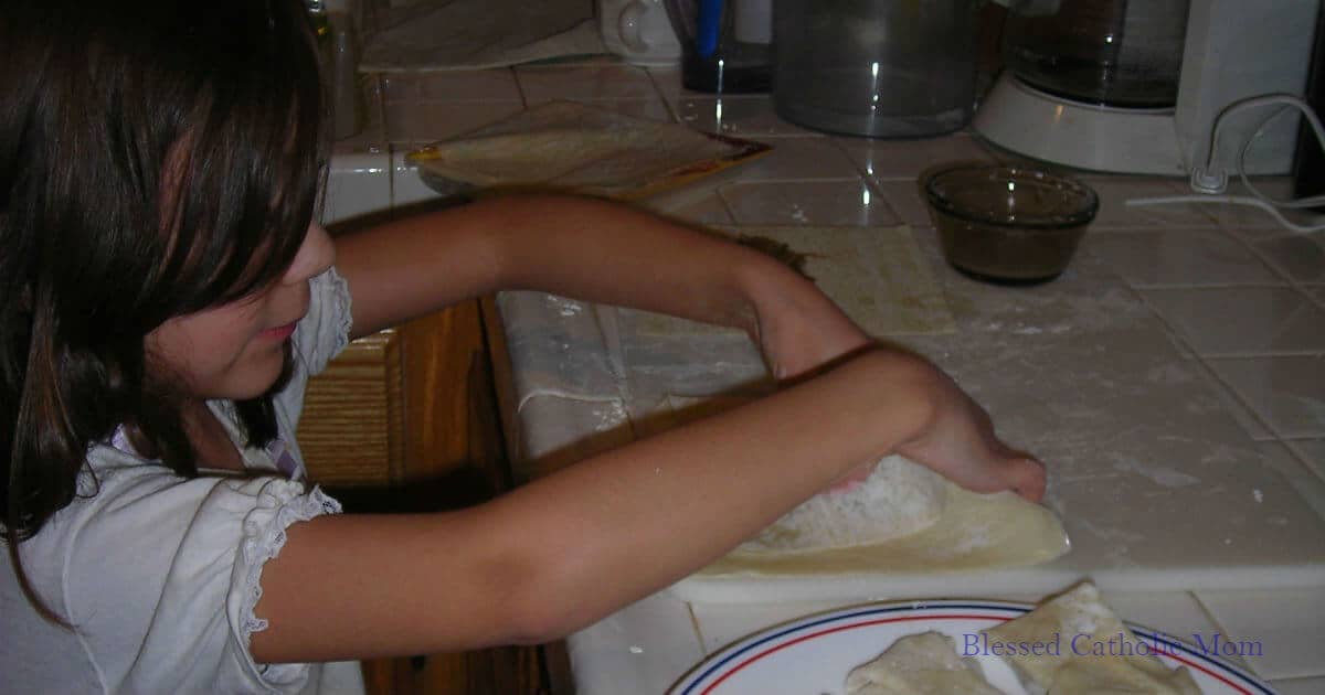 Image of a girl rolling egg rolls while standing at the kitchen counter.