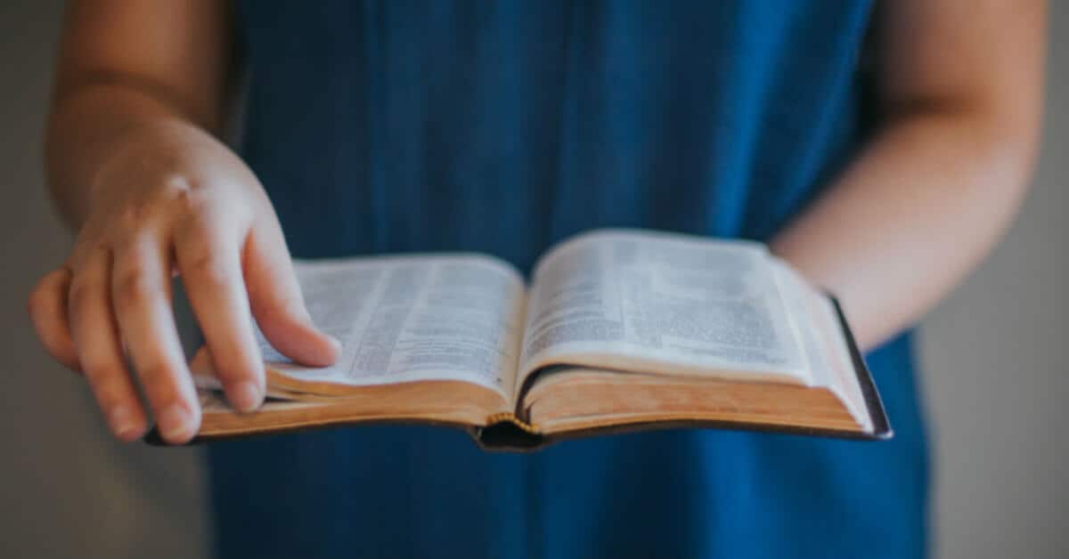 Image of two hands holding an open Bible. One hand is about to turn a page.