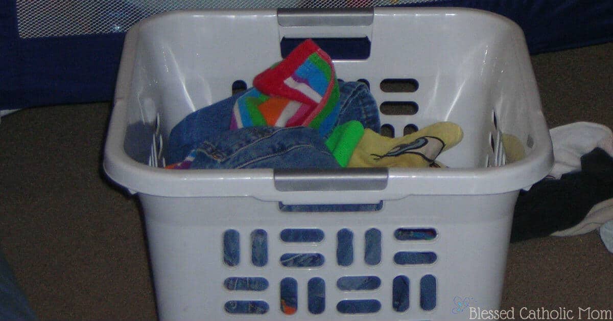 Here is a simple solution to our family's laundry dilemma: kids can do their own laundry. When we work as a family, we share the work load. Image of a white basket full of laundry. Blessed Catholic Mom logo on image. 