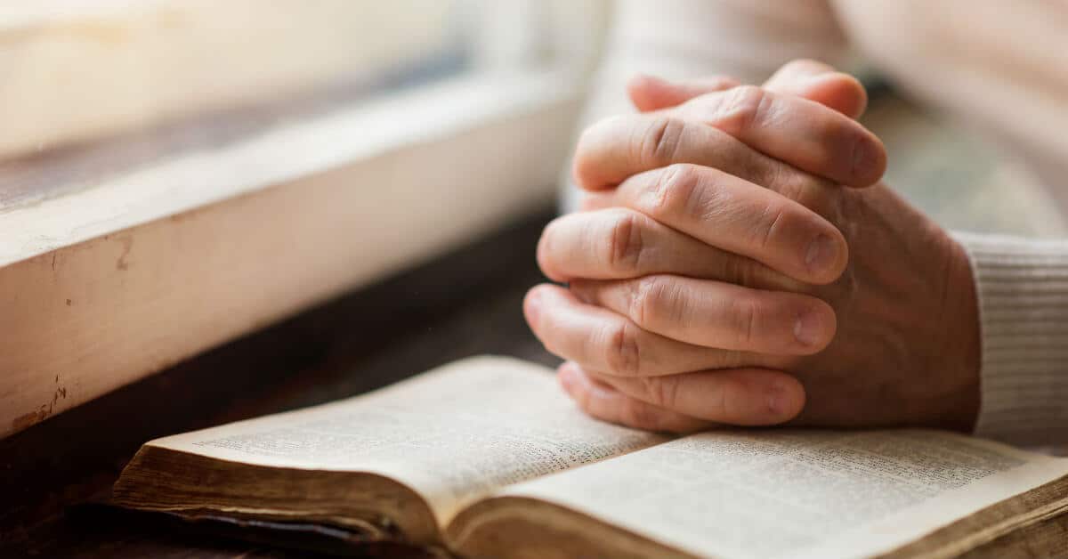 Learning how to pray in the way of Lectio Divina is not difficult. It is a way of prayer that helps to bring us closer to God. Here are the five simple steps to get you started. Image of a person sitting by a window, hands clasped together on top of an open Bible.