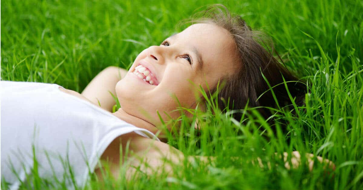God places dreams in our hearts that are uniquely suited to us. We do not have to fear them. Dream big and work every day to make those dreams a reality. Image of a young girl laying on her back on the grass, smiling and looking up at the sky.