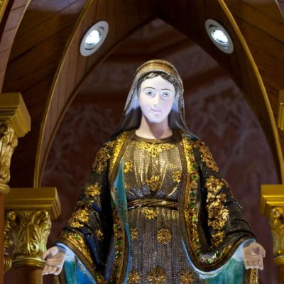 Image of a statue of Mary in a church, her arms outstretched towards us.