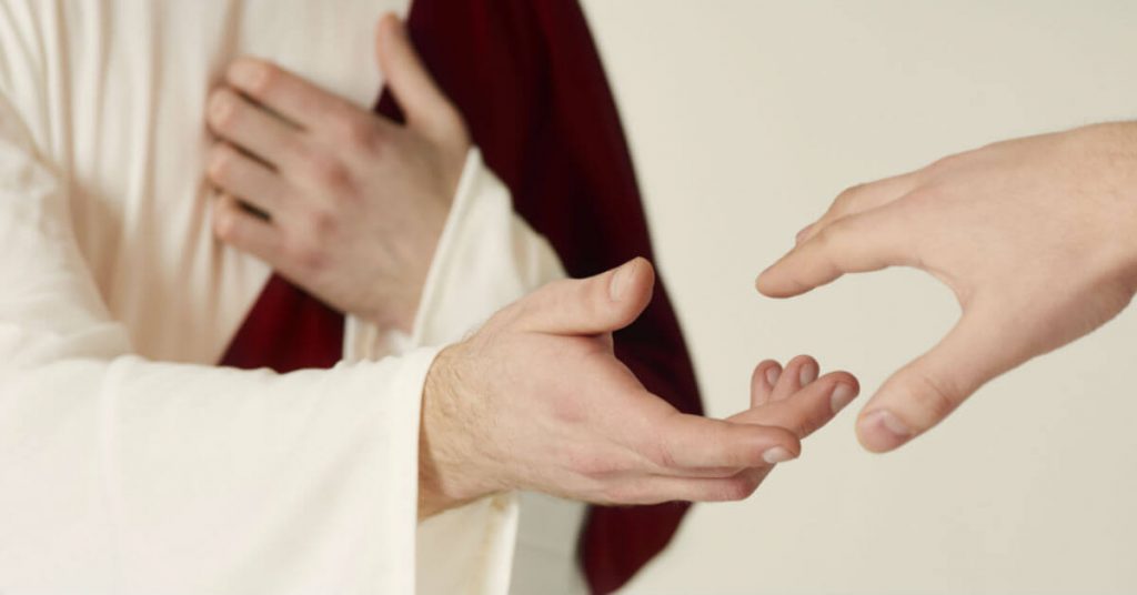 Image of a person representing Jesus holding out his hand to a person who si holding out his hand to Jesus.
