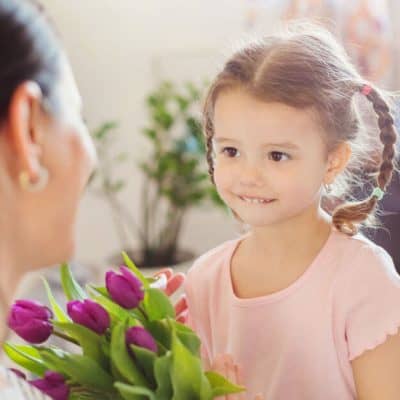 Image of a little girl giving purple tulips to her mother.