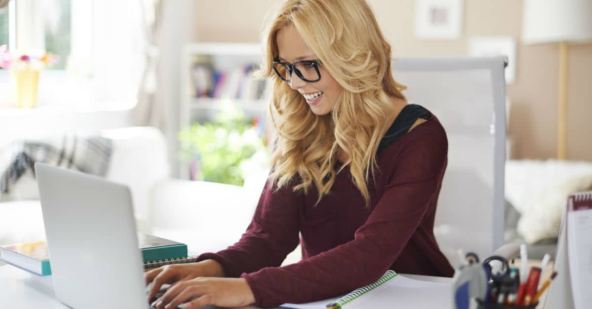 Image of a blonde woman with glasses using a laptop at home.
