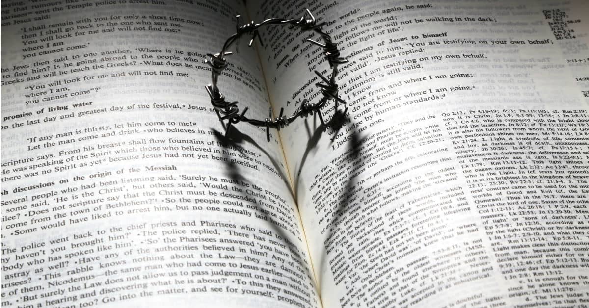 Image of a small metal crown of thorns on top of an open Bible. The shadow of the crown on the Bible is in the shape of a heart.