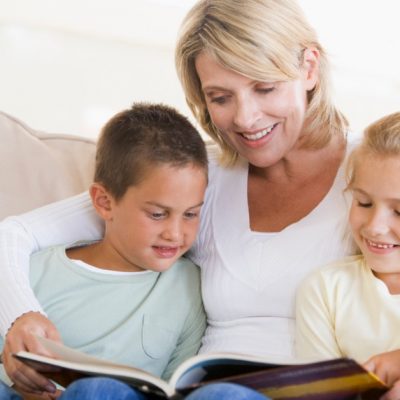 Image of a mom sitting with her son and daughter reading together.