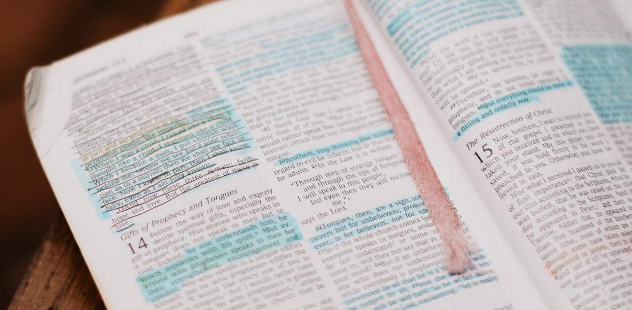Image of an open Bible on a table. The pages have passages highlighted in blue and underlined in black.