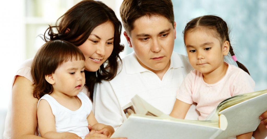 Image of a family-Dad, Mom, son, and daughter-reading a book together.
