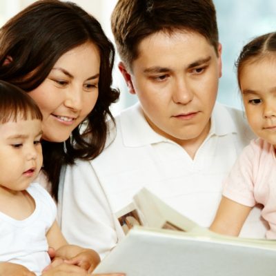 Image of a family-Dad, Mom, son, and daughter-reading a book together.