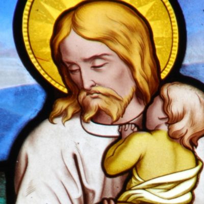 Image of a stained glass window of Jesus holding a little child in His arms.