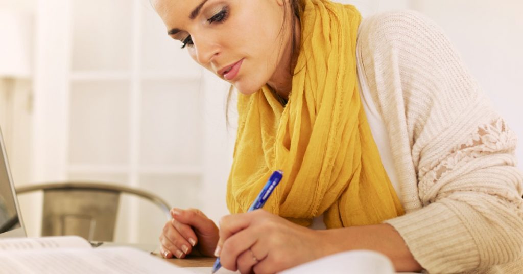 Image of a woman sitting at a desk writing something on a piece of paper.