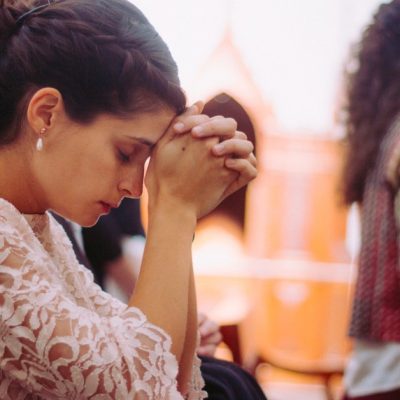 Image of a woman kneeling in prayer in church.