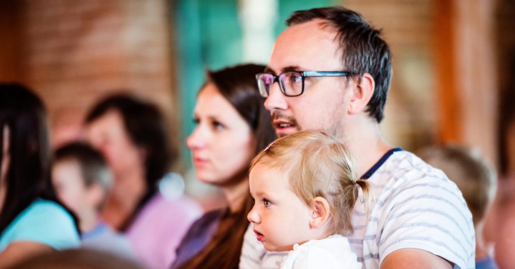 Image of a Dad holding his daughter sitting beside his wife at church together.