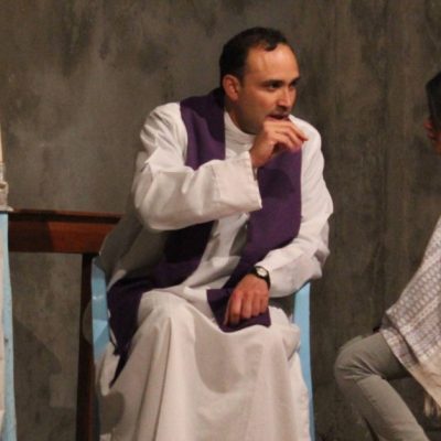 Image of a priest and a woman sitting down in Church, facing each other as the priest hears the woman's Confession.