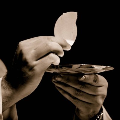 Image of a priest holding up the Eucharist-Body of Christ.