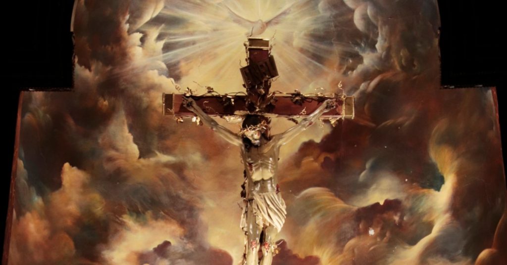 Image of Jesus crucified. He is surrounded by images of clouds and the Holy Spirit as a dove is above the cross.
