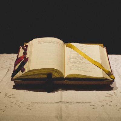 Image of an open Bible on a table with a lit candle on each side of it.