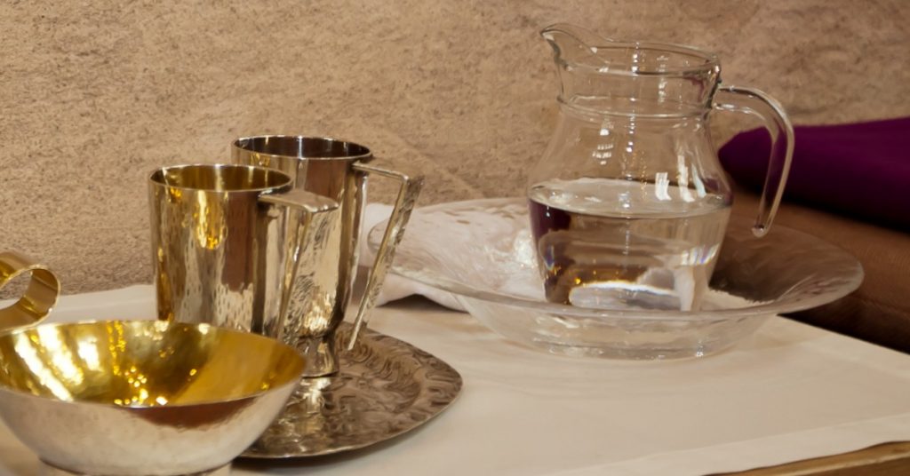 Image of two gold chalices, a small clear pitcher of water, and a bowl for the priest to use for Catholic Mass. While the priest is washing his hands, the faithful can silently pray the Catholic Prayer at the Ablution.