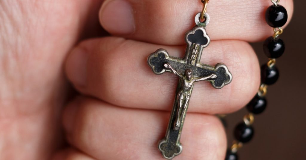 Image of a hand holding a Rosary with the crucifix showing. 