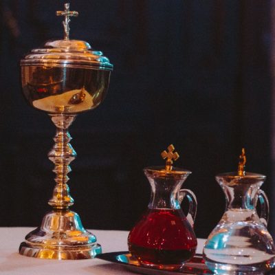 Image of the offertory gits: a gold ciborum beside tow containers with wine and water awaiting the offertory at a Catholic Mass.