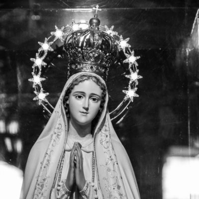 Image of a statue of Mary the Mother of God, her hands clasped in prayer, crowned as Queen of Heaven and earth with a ring of stars around her head.