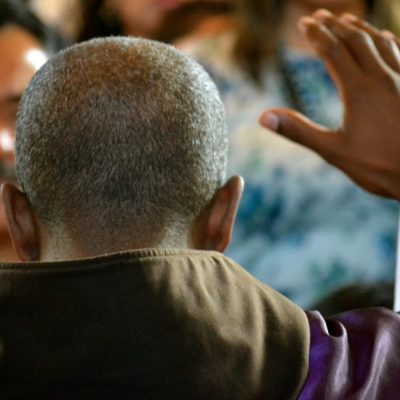 Image of a Catholic priest with his back to the camera raising his hand in blessing in front of the people at Mass.