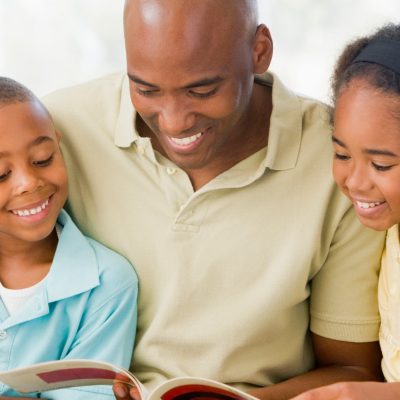 Image of a father smiling as he reads to his son and daughter.