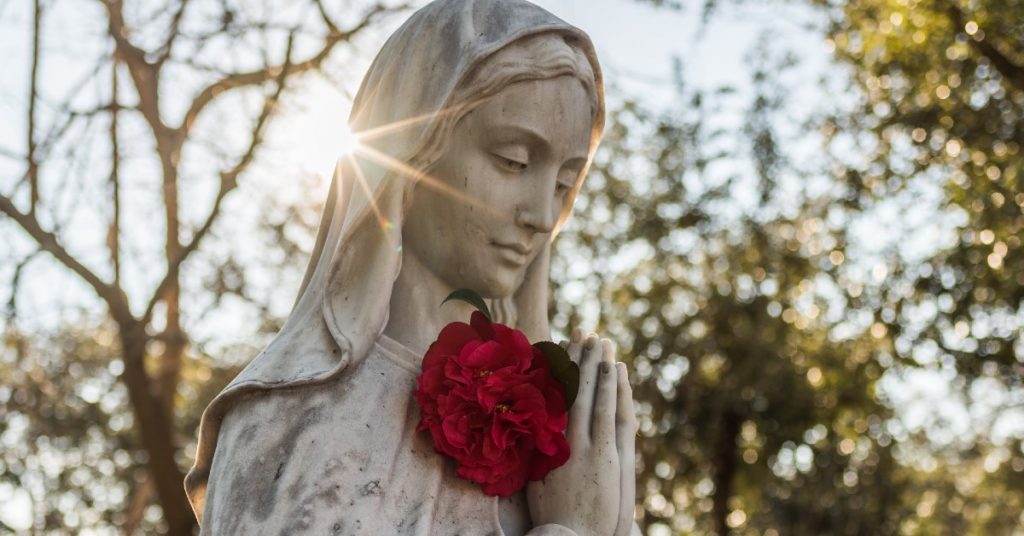 Image of a white statue of the Blessed Virgin mary our Mother with red roses in her hands.