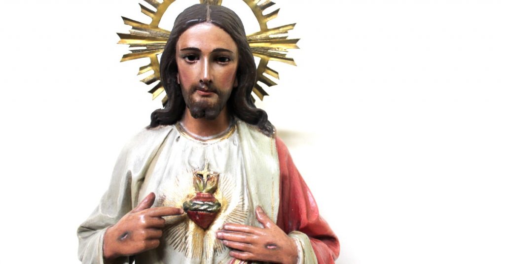 Image of a statue of Jesus wearing a golden halo and pointing to His Sacred Heart with His pierced hands.