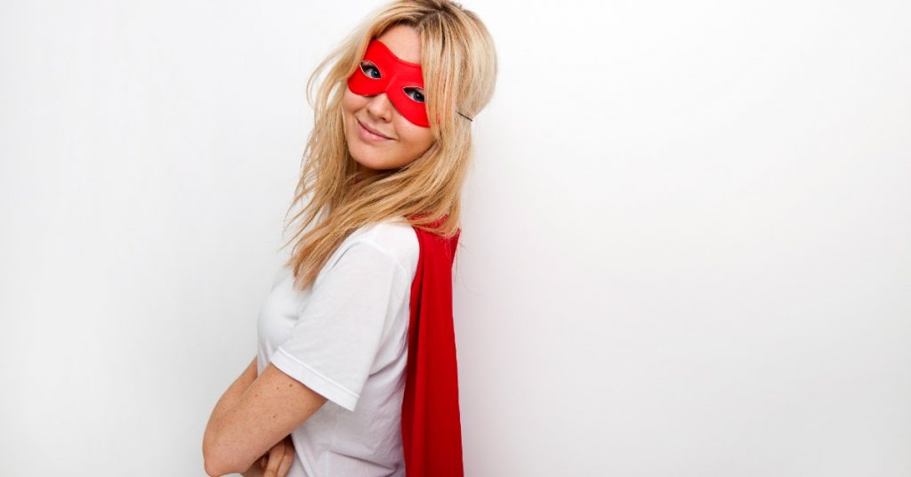Side view portrait of a confident woman in superhero costume of a red mask and a red cape against white background.