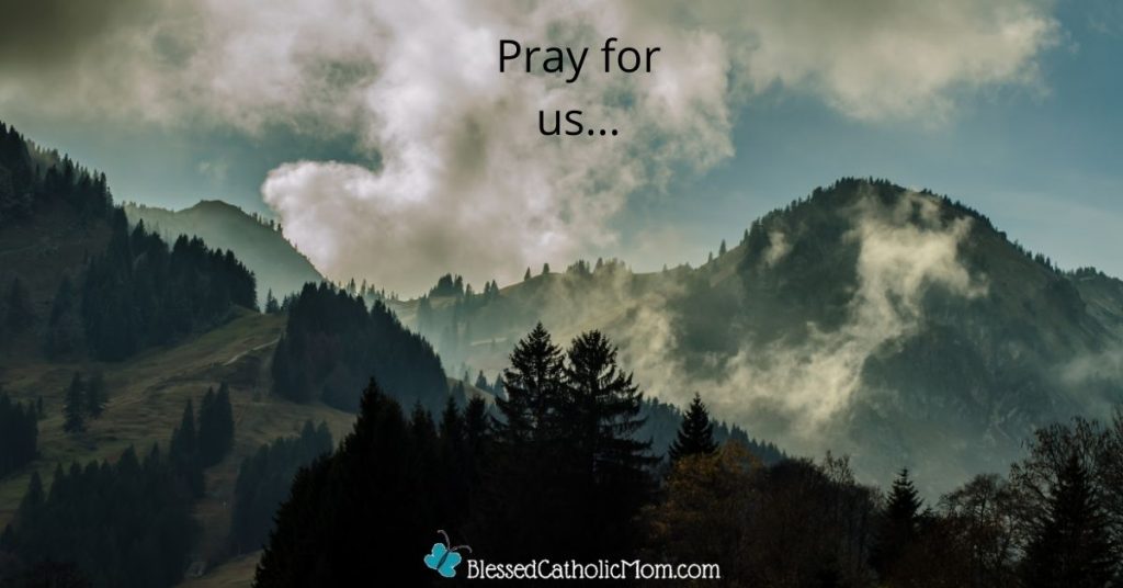 Image of mountains wiht pine trees on them and white clouds above them. The words Pray for us... are at the top of the image and the logo for Blessed Catholic mom dot com is at the bottom.