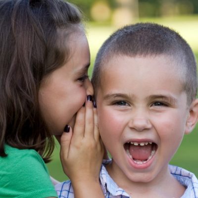 Image of a young girl whispering in the ear of her younger brother to tell him a secret.