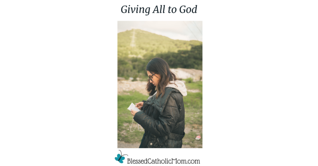 Image of a young woman outside by a foothill wearing a heavy black coat reading from the paper in her hand while she holds a Rosary. Giving All to God are the words above the image and the logo for Blessed Catholic Mom is below.